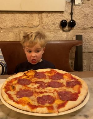 A 4 year old, sat in front of a giant pizza. His mouth is wide open in awe